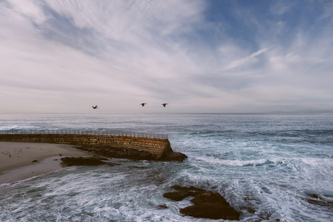 brown concrete fence beside sea waves under white clouds at daytime