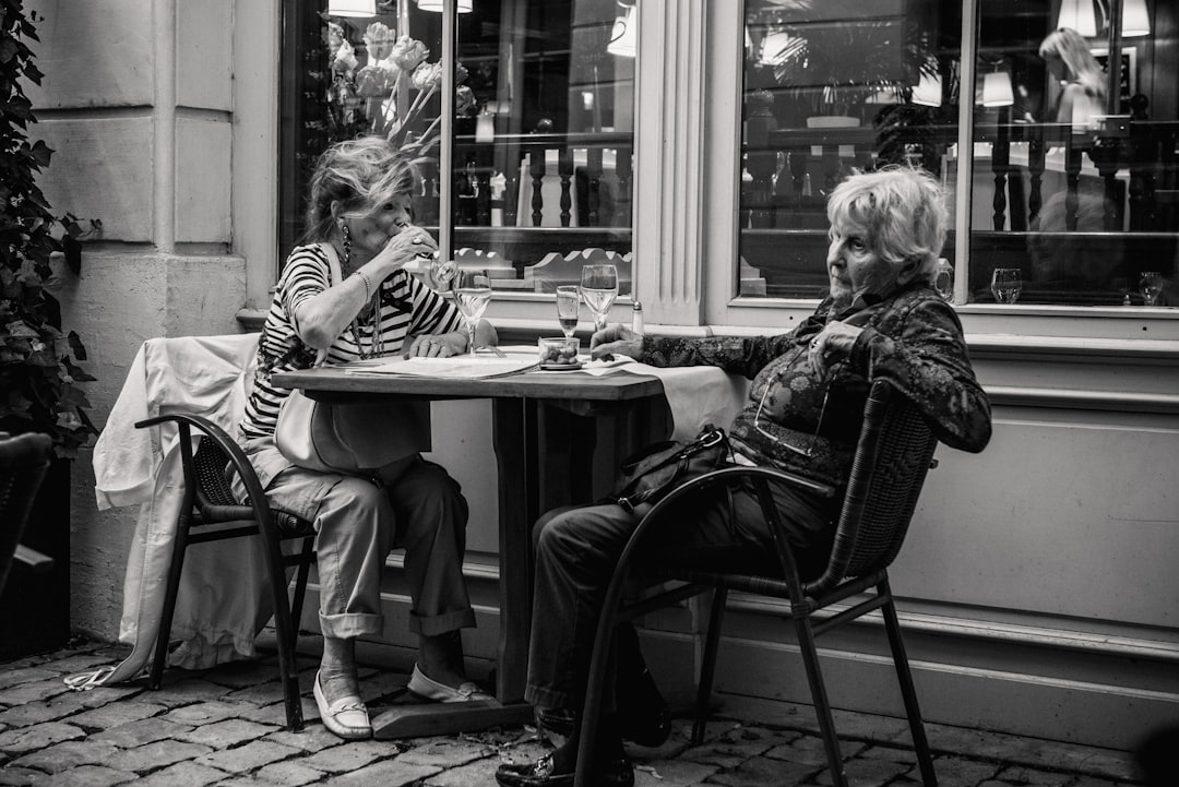 grayscale photo of two woman sitting beside the table