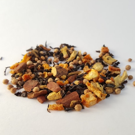 A variety of dried spices and herbs scattered on a white surface, including pieces of cinnamon, ginger, coriander seeds, and other colorful ingredients.