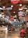 A vintage-themed interior display featuring an array of classic cars, wagons, and bright neon signs hanging from a wooden ceiling. The signs include logos and brand names related to automobiles and the transportation industry. The floor is polished, reflecting the warm light from the fixtures above.