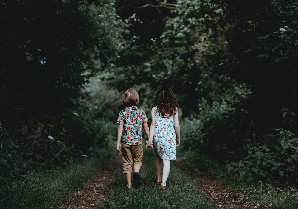Menino e menina caminhando de mãos dadas em direção à floresta