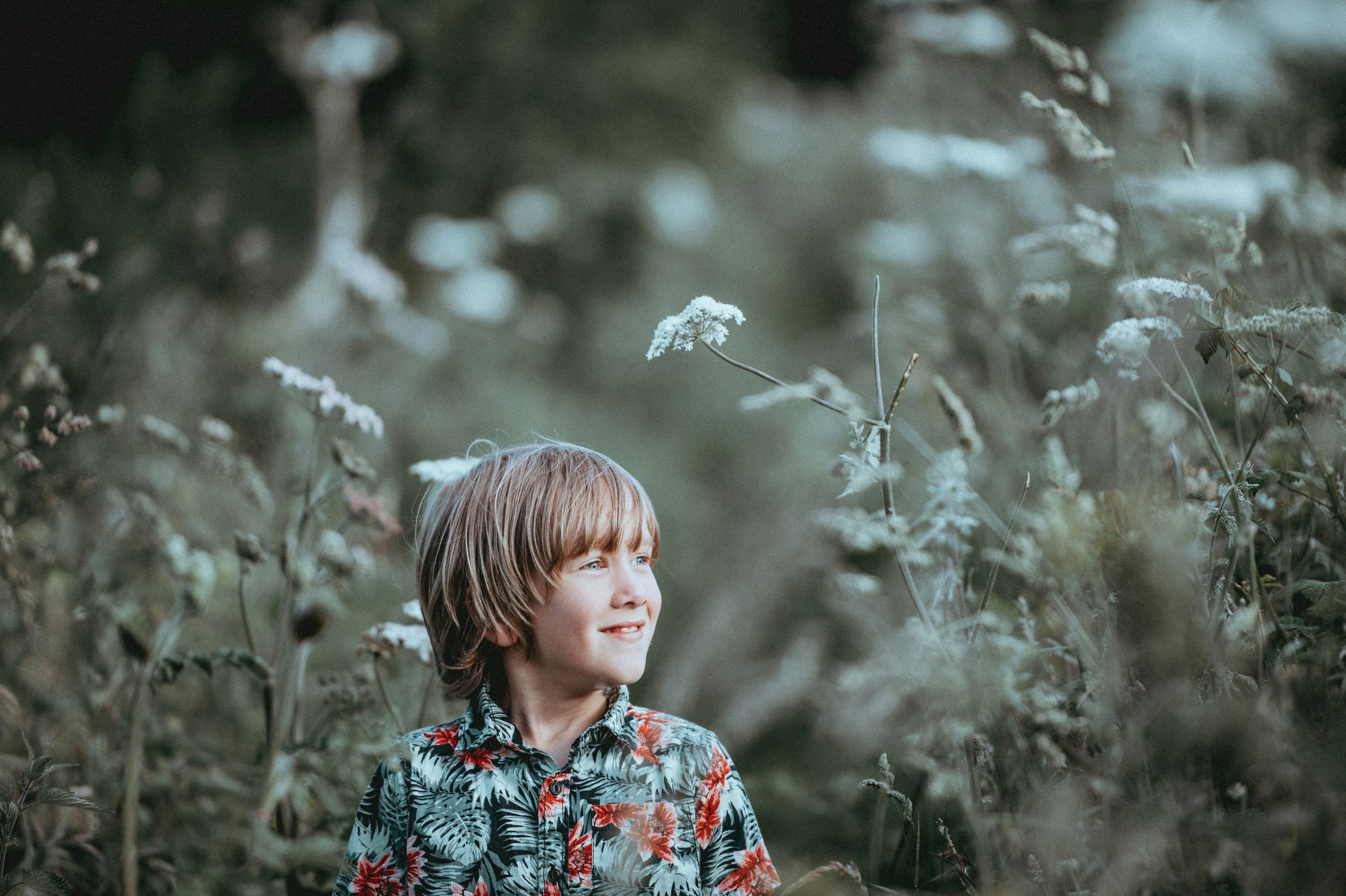 boy's red and green floral button-up collared top smiling facing grasses