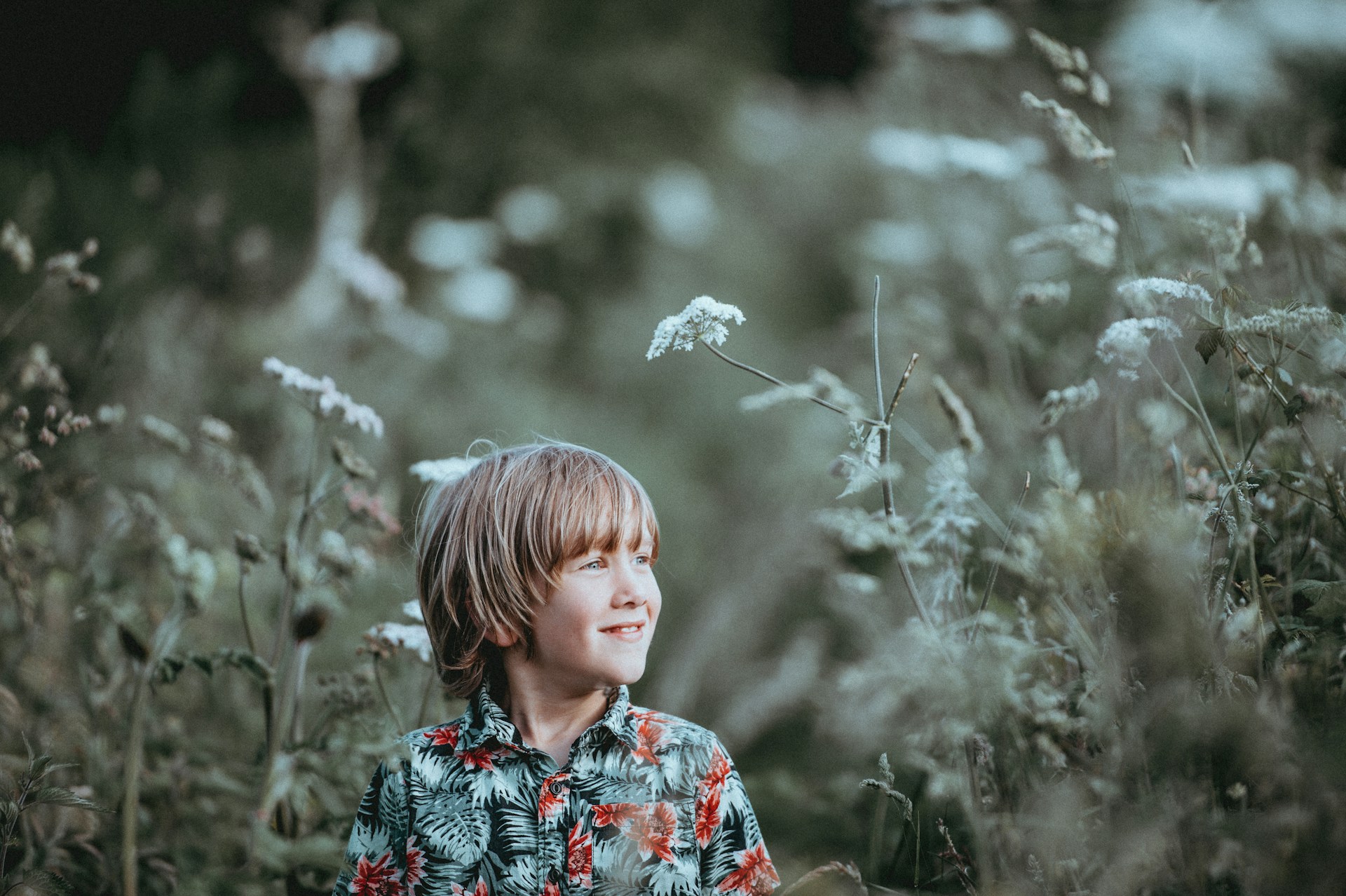 boy's red and green floral button-up collared top smiling facing grasses