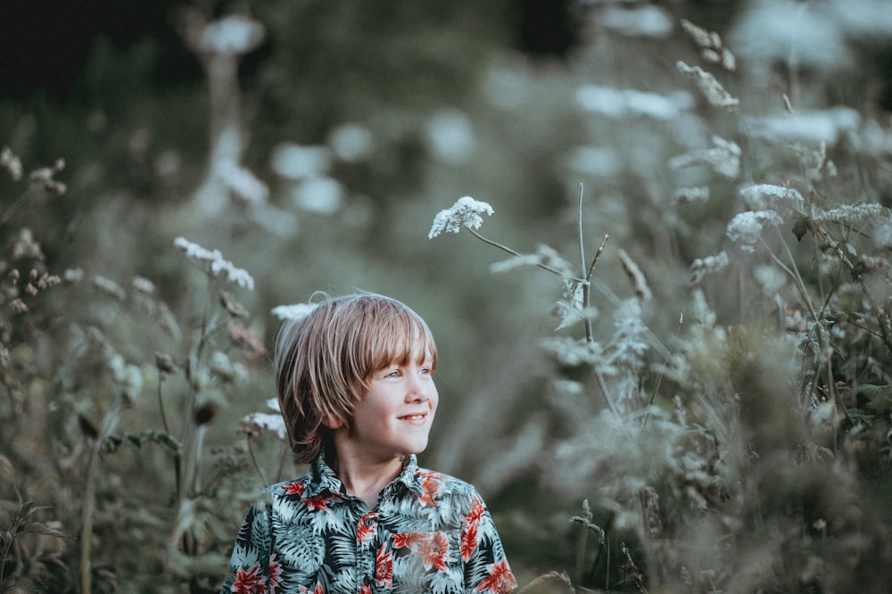 boy's red and green floral button-up collared top smiling facing grasses