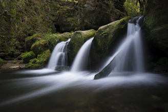 A tranquil waterfall cascading over moss-covered rocks in a lush forest setting, capturing the serene beauty of nature.