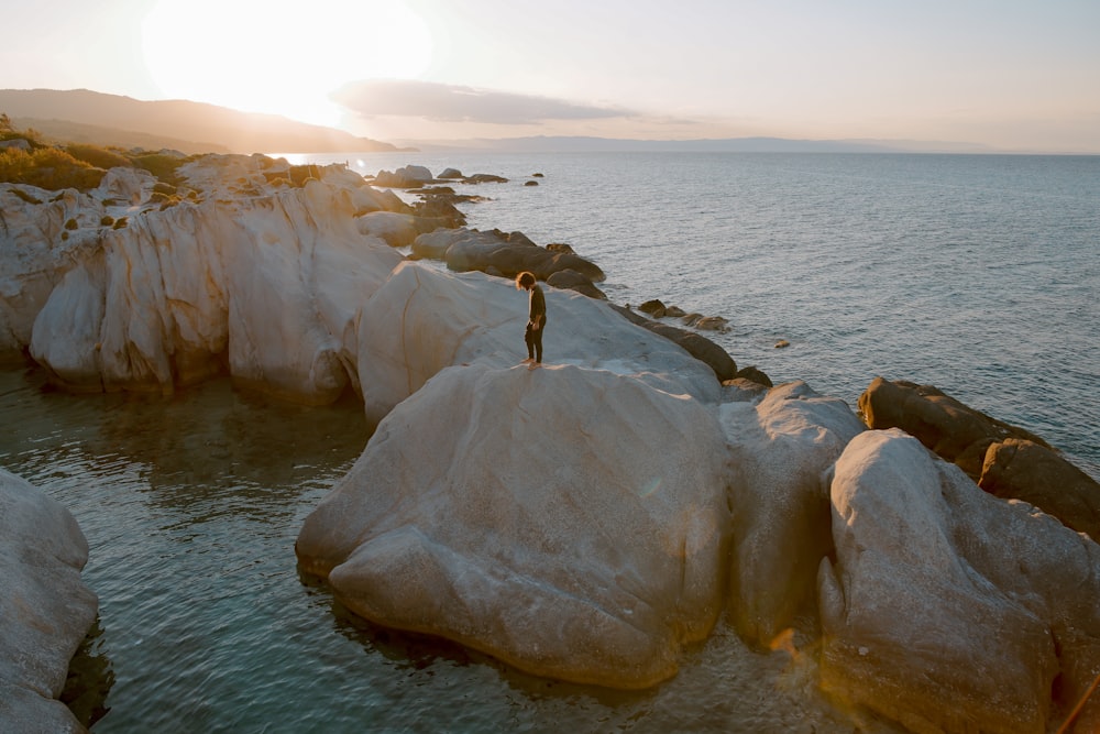 水に囲まれた茶色の岩の上に立つ人の写真