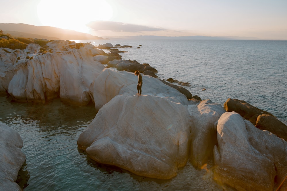 photo of person standing on brown boulder surrounded by water