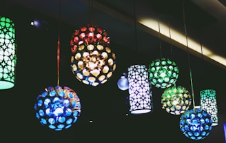 Several hanging lamps feature intricate, colorful designs with circular and patterned motifs. The lamps emit a soft, colorful glow creating a vibrant atmosphere against a dark background.