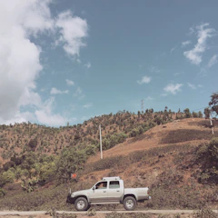 Silver pickup truck hauling a small piece of machinery on a rural road.