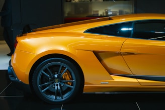 A sleek, high-performance sports car in a vibrant orange color is showcased, highlighting its aerodynamic design and black alloy wheels. The image captures the side view of the vehicle, emphasizing the contours and aggressive styling typical of luxury supercars.