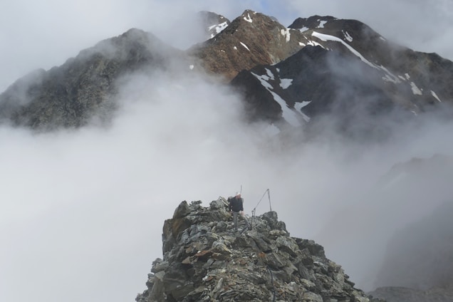 A rugged hiker standing on a rocky outcrop overlooking a misty Canadian mountain valley at dawn.