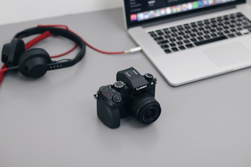 A black camera sitting on a desk next to a laptop and headphones.