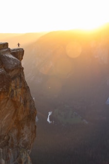 silhouette of person standing on cliff during sunset