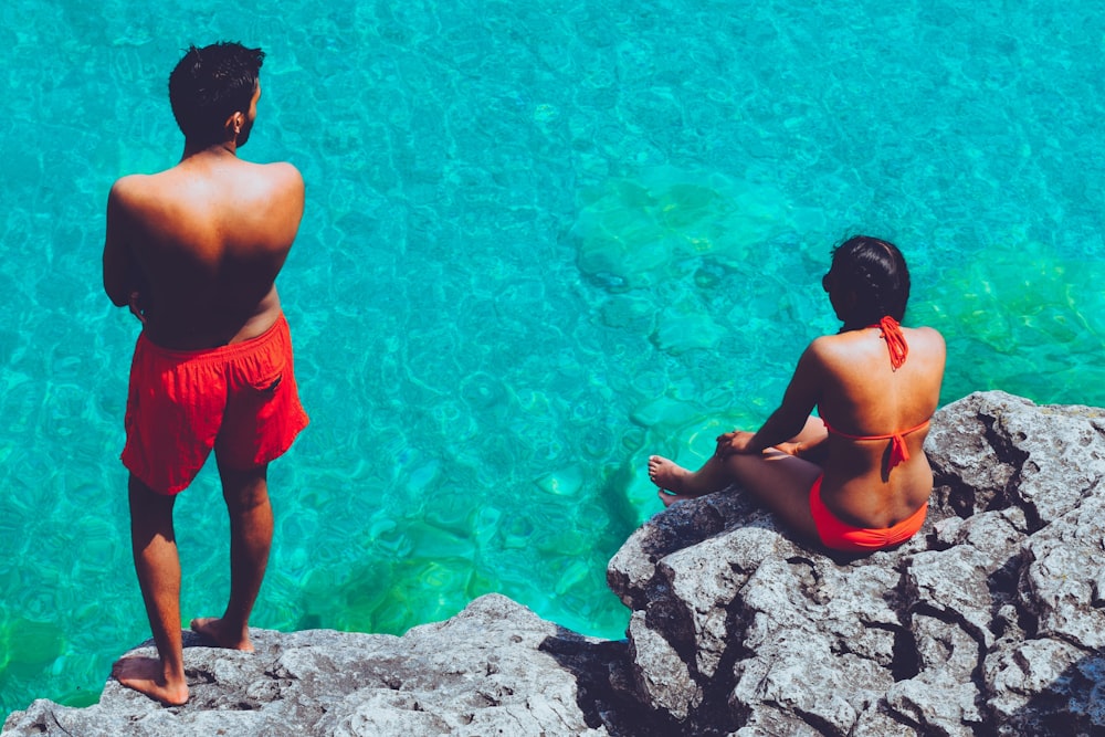 Homem e mulher sentados em rocha perto do corpo de água