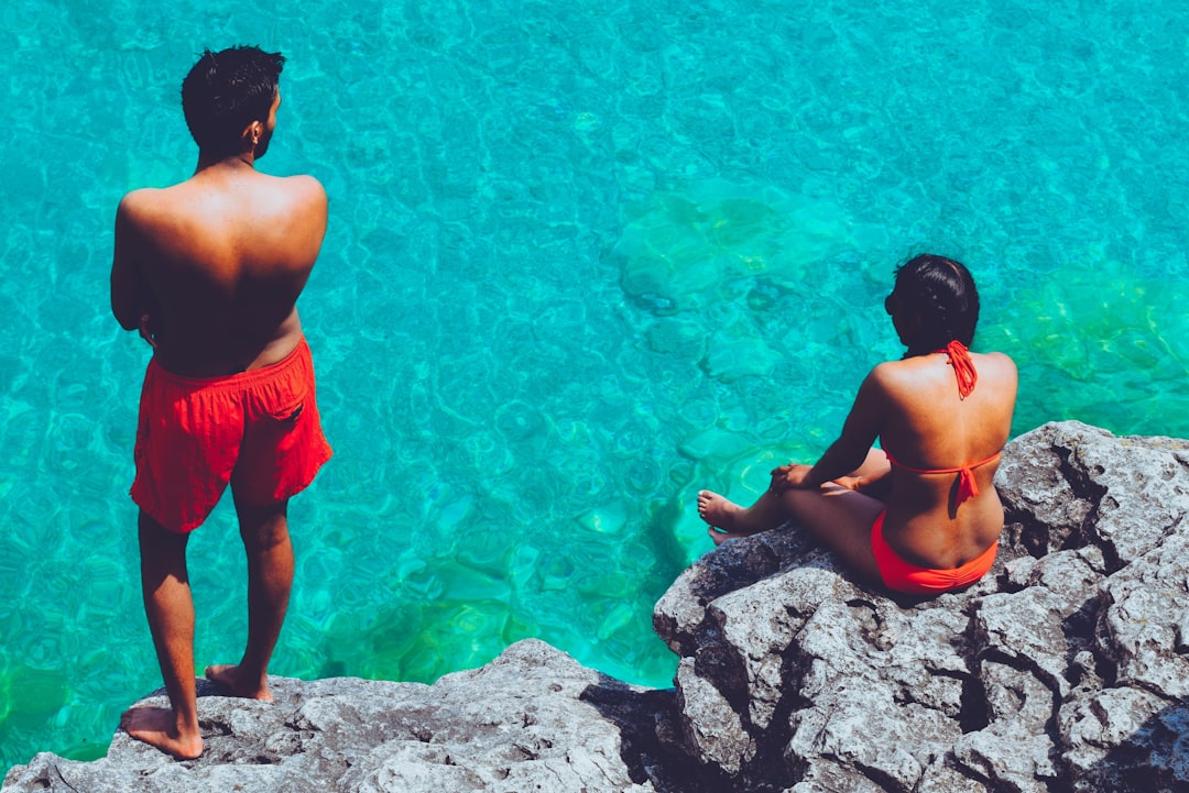 man and woman sitting on boulder near body of water