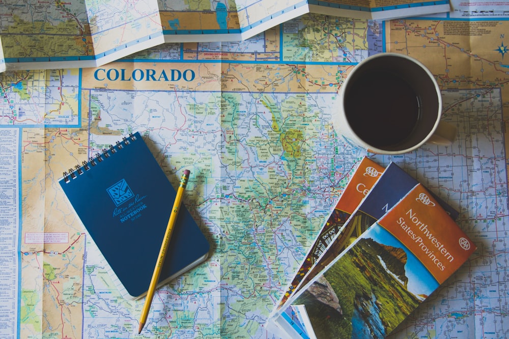Rite in the Rain notebook, coffee, pencil, and three atlases sit on a map of Colorado