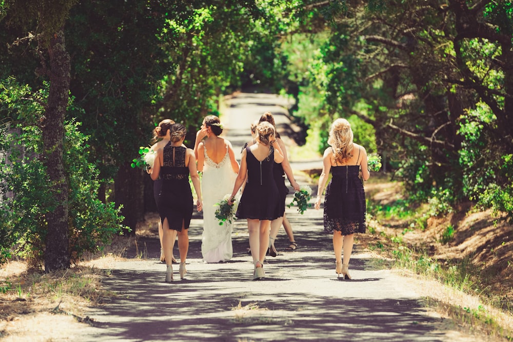 bride and bridesmaid walking on street between green trees