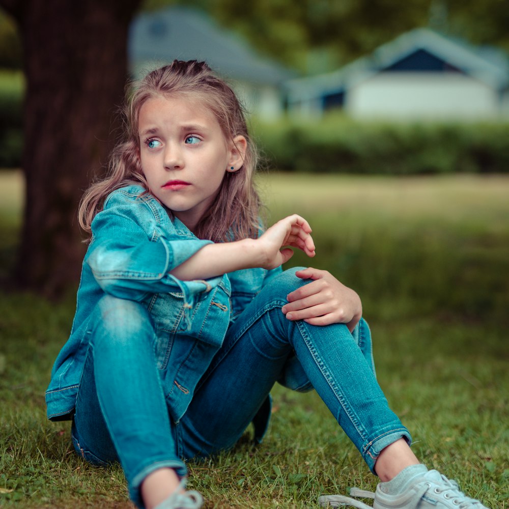 Photographie sélective de mise au point d’une fille assise près d’un arbre