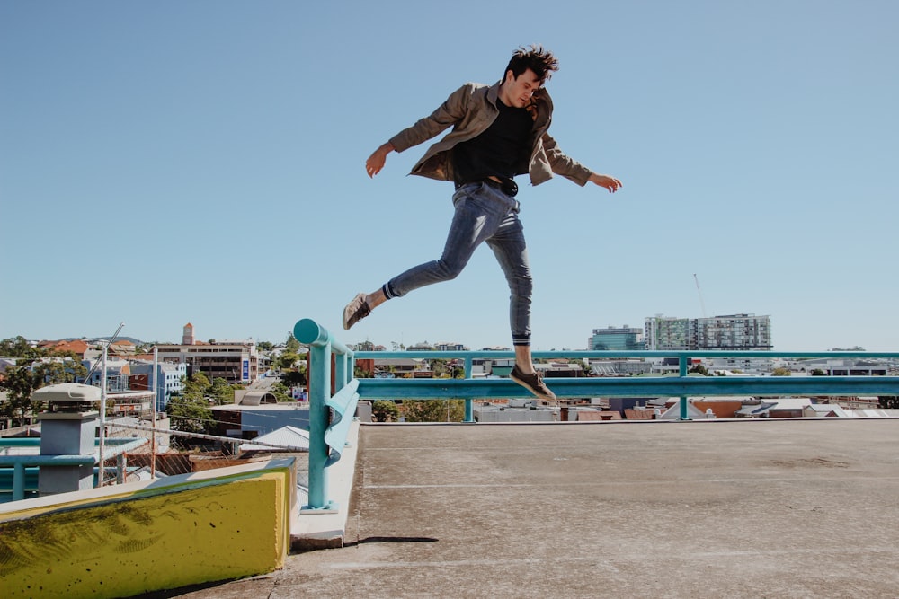 Un homme saute d’une clôture bleue à un trottoir en béton brun
