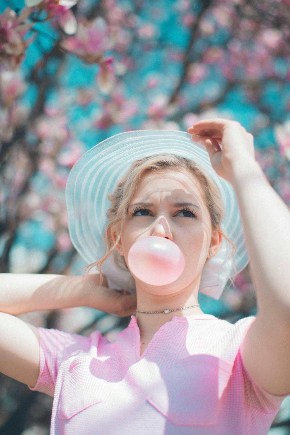 woman under pink tree blowing chewing gum