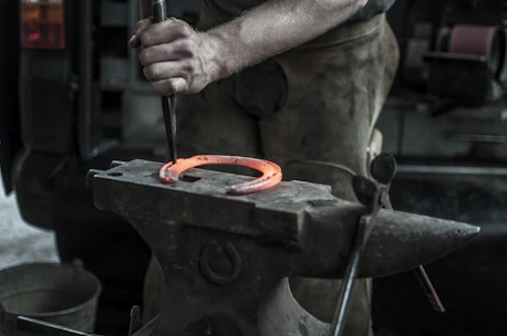 Close-up of a skilled farrier shaping a horseshoe with traditional tools in a rustic workshop.