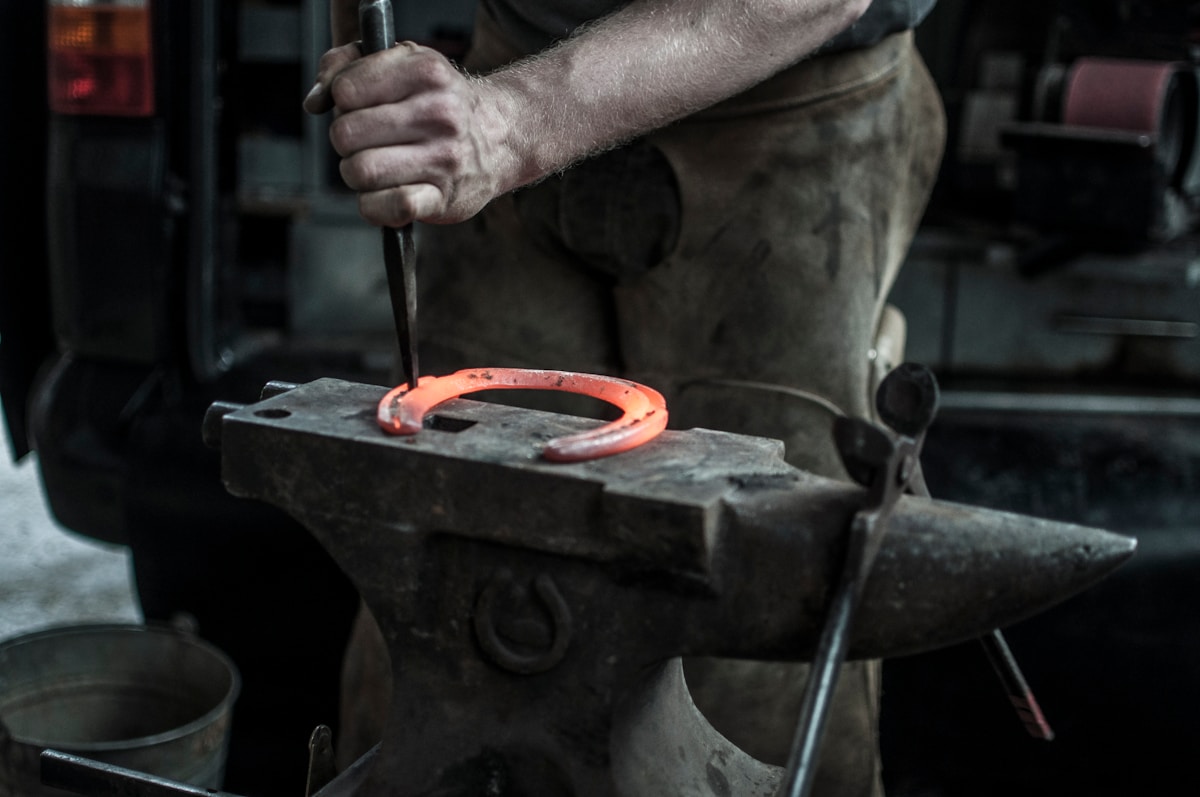 Photograph of a man working on a red hot horseshoe on an anvil.