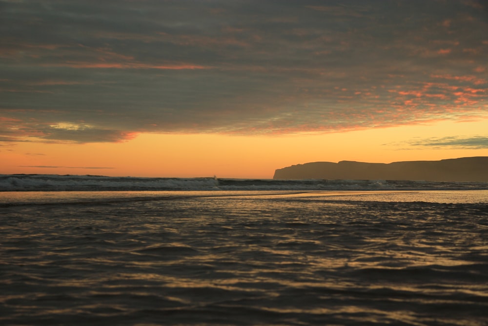 calm body of water near mountain at golden hour