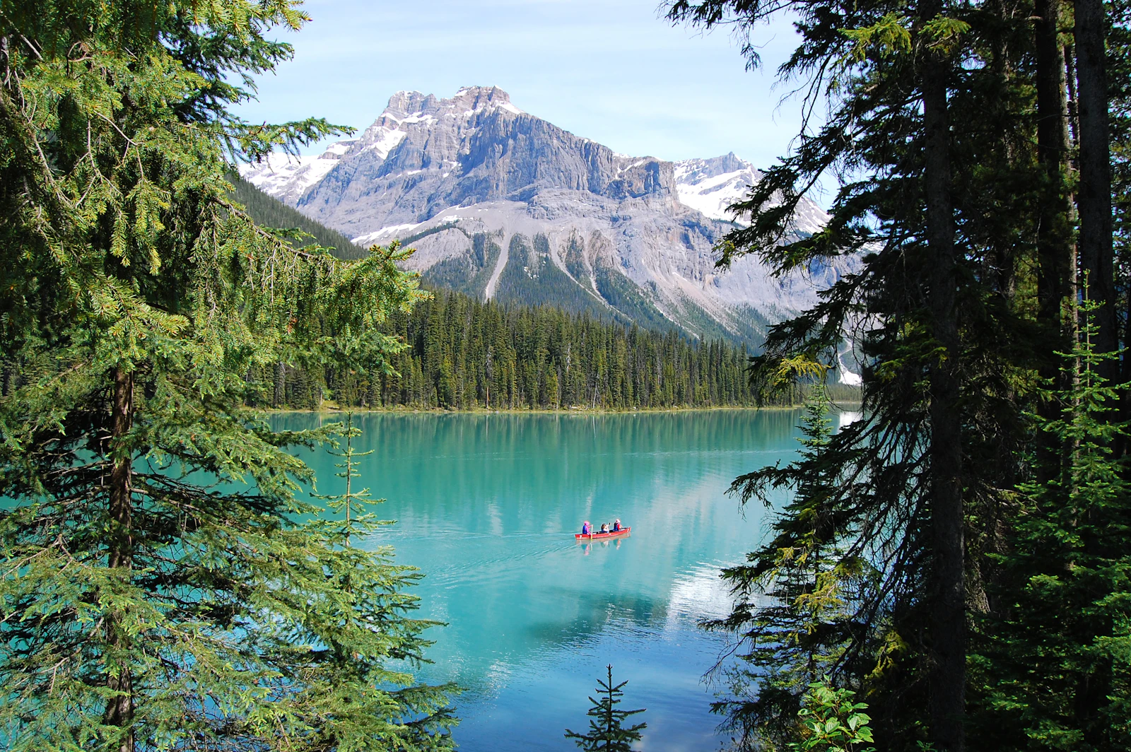 A red canoe on the turquoise water of Emerald Lake framed by evergreens below a Canadian Rocky Mountain peak