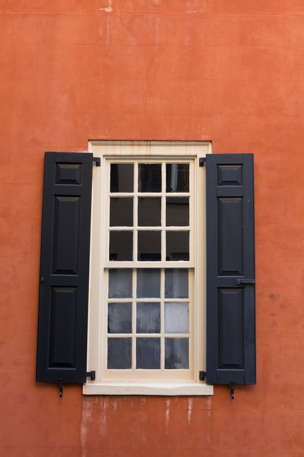 a window with black shutters on a red wall