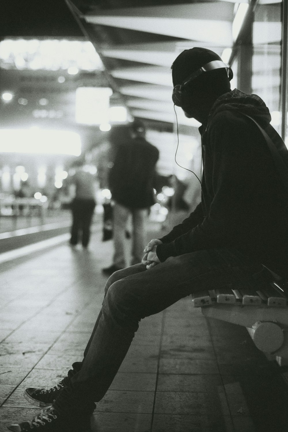 fotografia em tons de cinza de um homem sentado no banco enquanto ouve música