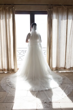 A flowing ivory wedding dress hanging by a sunlit window.