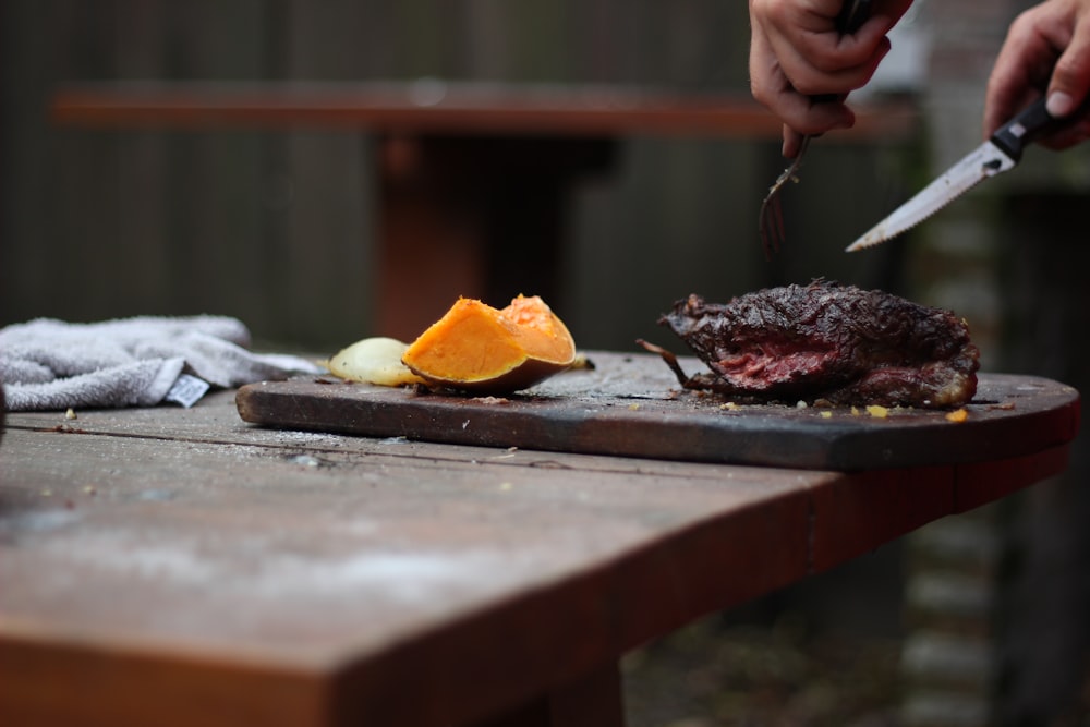 person slicing a meat using knife and fork