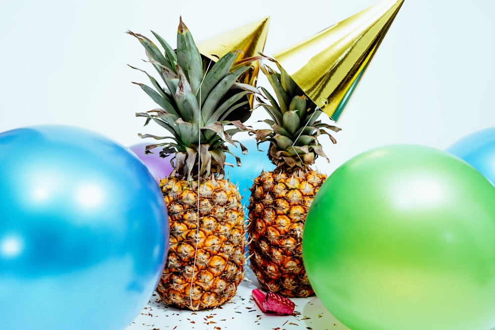 due ananas con cappelli da festa d'oro vicino a palloncini colorati