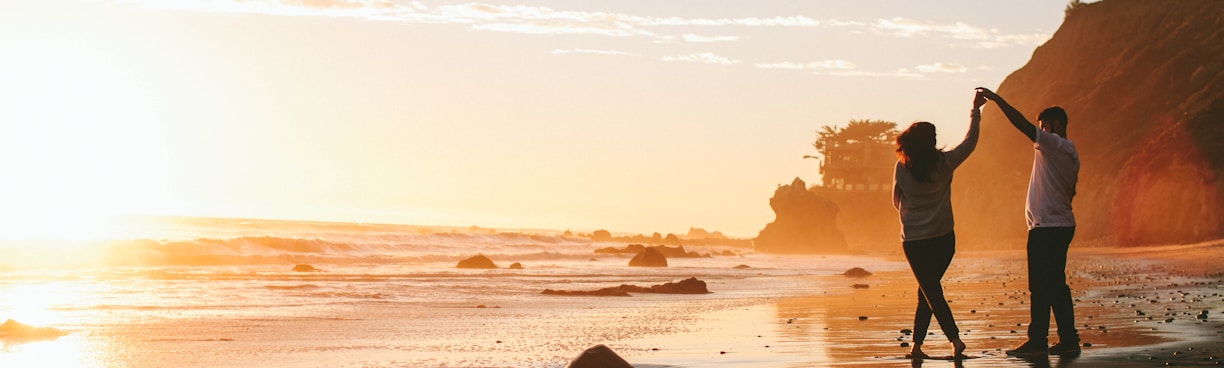 woman and man holding hands while standing on shore during golden hour