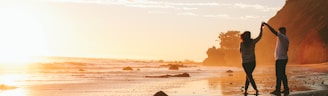 woman and man holding hands while standing on shore during golden hour