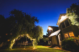 A warm evening scene showing a cozy home and garden softly lit by solar-powered lights under a clear sky.