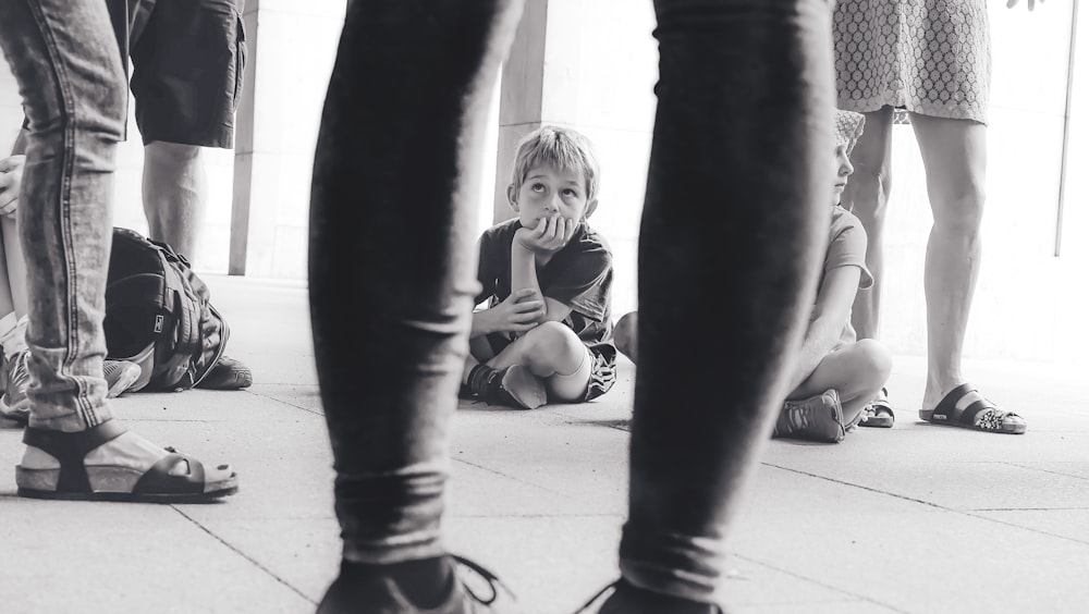 fotografia em tons de cinza do menino sentado no chão observando a pessoa à sua frente
