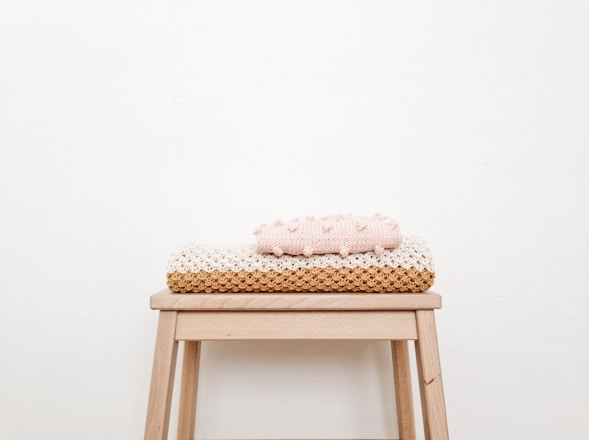 A cozy, folded minimalist blanket in soft muted tones draped over a simple wooden chair.