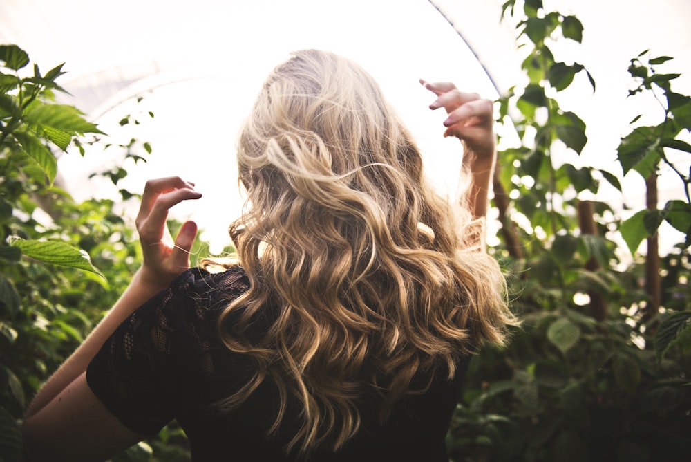 femme aux cheveux blonds en haut noir entourée de grandes plantes