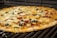 A pizza with a golden-brown crust is topped with melted cheese, black olives, green bell peppers, red bell peppers, and slices of pepperoni. The pizza appears to be cooking on a grill.