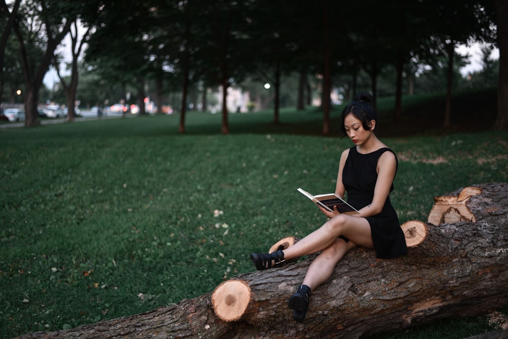 woman reading book while sitting on fallen tree trunk