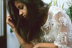 A person with long hair is wearing a translucent, floral-patterned garment. The setting includes some greenery in the background, adding a natural element.