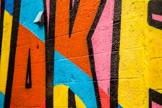 A vibrant wall mural featuring bold geometric shapes with thick black outlines. The mural includes large sections of various colors painted on a textured brick surface.