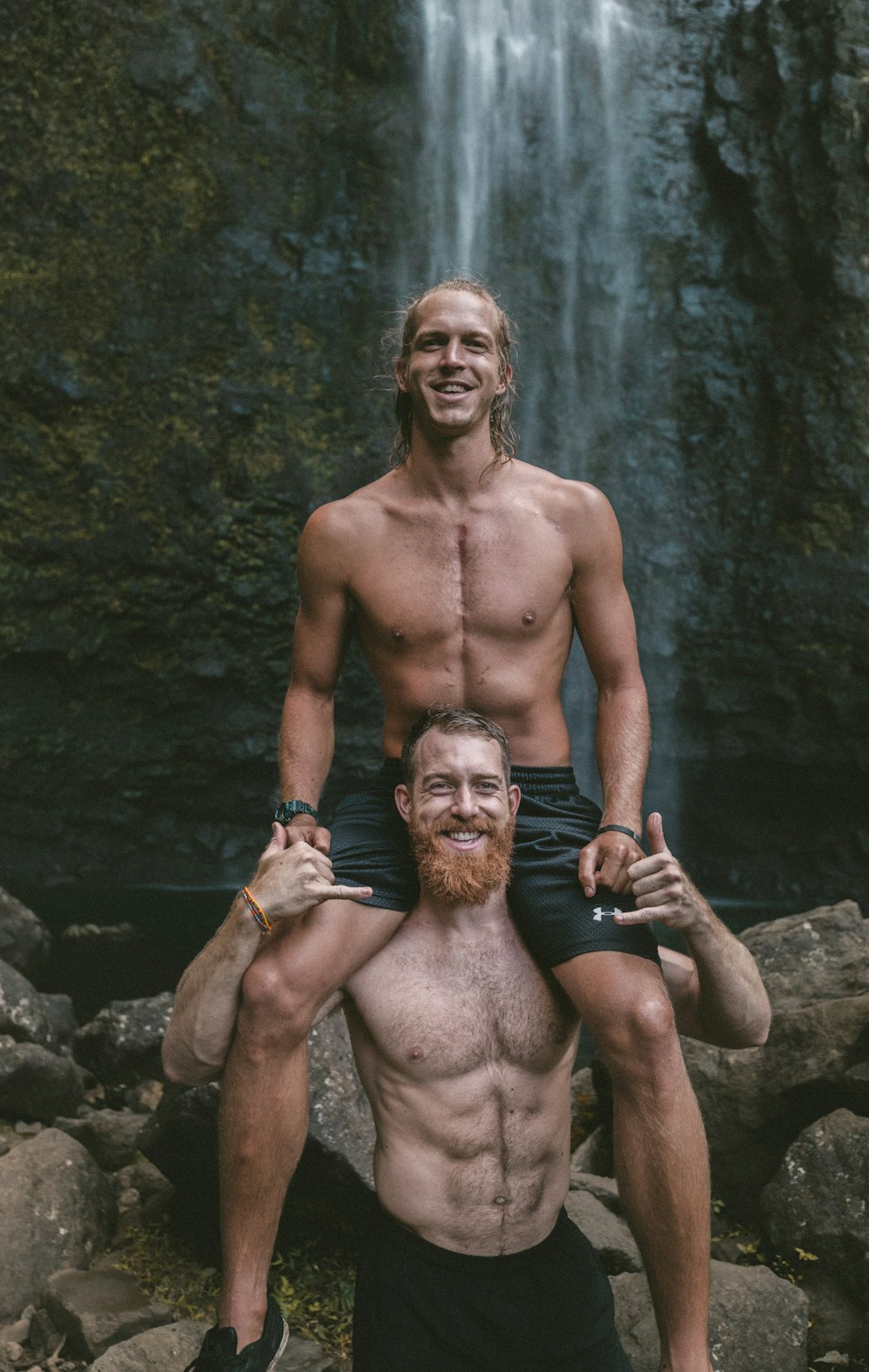 a man is holding a man on his shoulders in front of a waterfall
