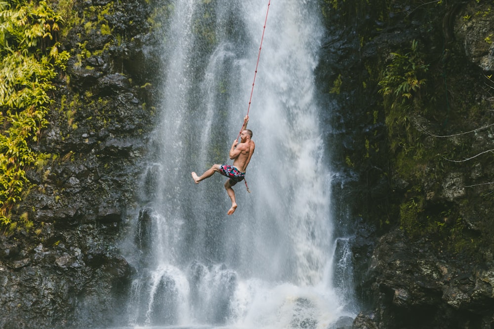 homme suspendu à une corde près des chutes d’eau pendant la journée