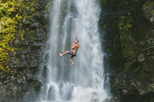 man hanging on rope near waterfalls during daytime in Waimea United States