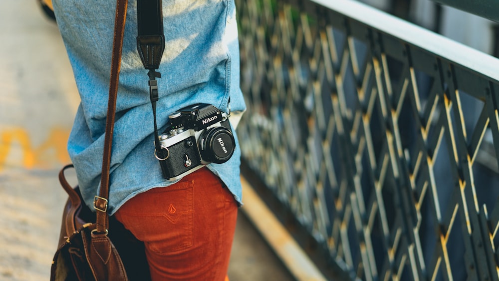 person carrying bag and camera facing fence