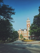 Close-up of the university's iconic red-brick clock tower framed by lush green trees under a clear blue sky.