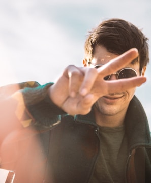 shallow focus photography of smiling man doing peace sign