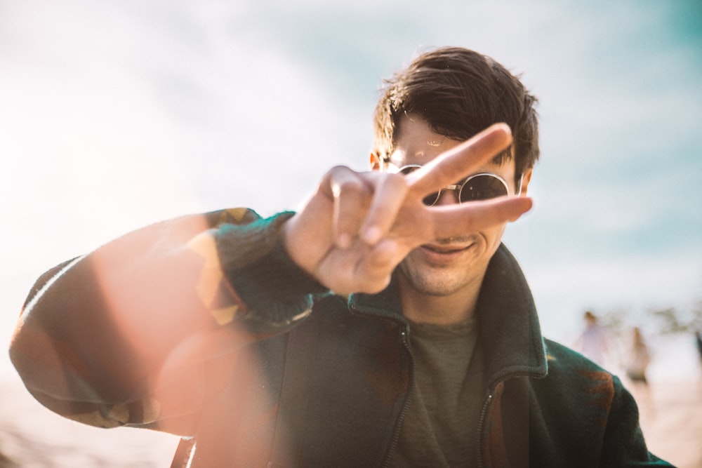 shallow focus photography of smiling man doing peace sign